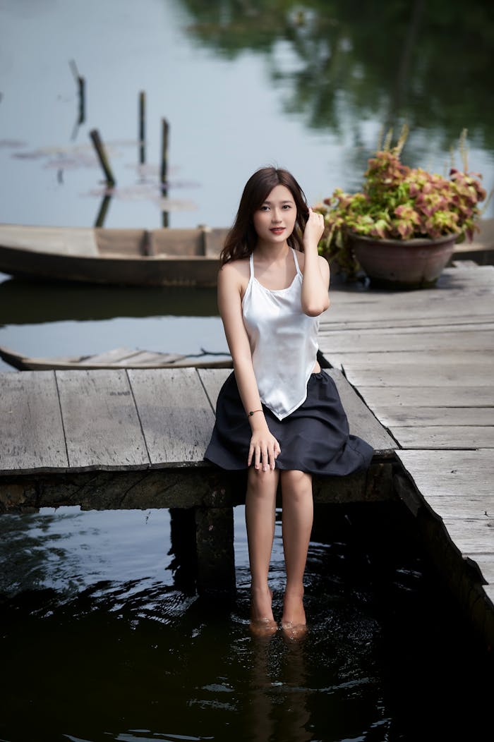 A serene portrait of a young woman sitting on a footbridge by a calm lake.